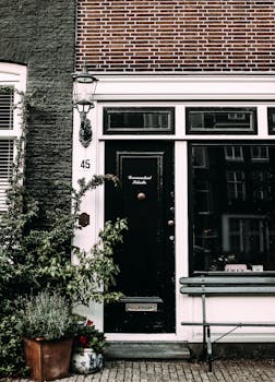 pexels-photo-4992778-4992778 Exterior of residential house with black door located on paved terrace with green potted plant streetlamp and bench on street